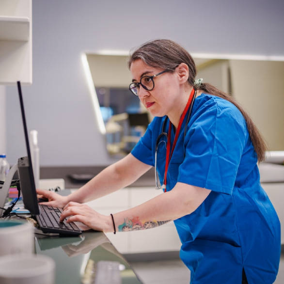 Zorgverlener met een blauw pak aan kijkt geconcentreerd naar een computerscherm in een behandelruimte